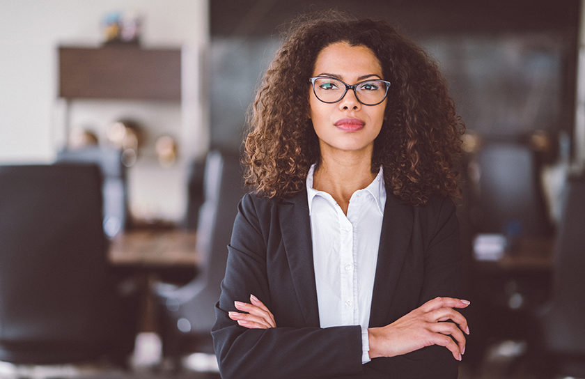professionally dressed woman in glasses standing up with arms folded