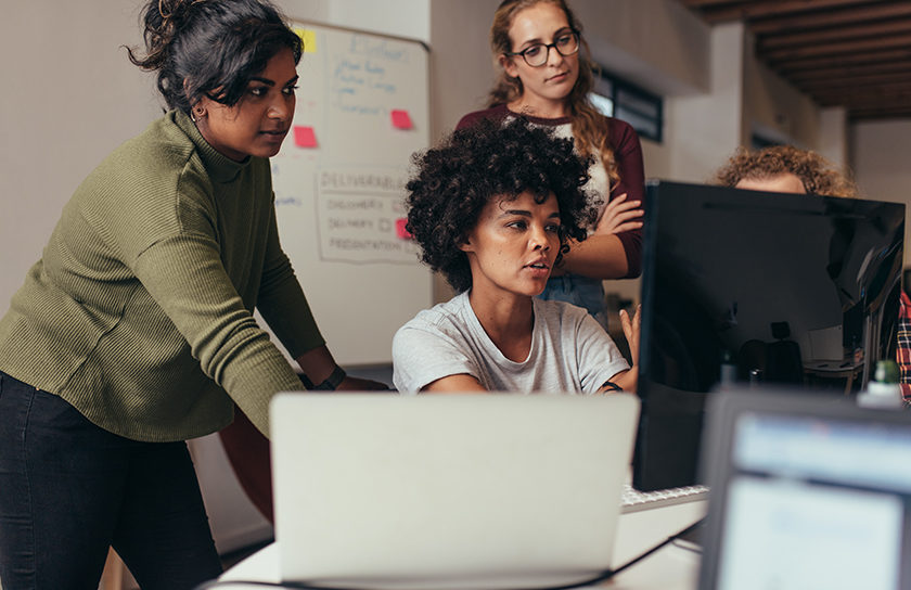 a group of young people working around a laptop computer