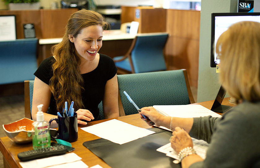 smiling woman at desk taking pen from another woman