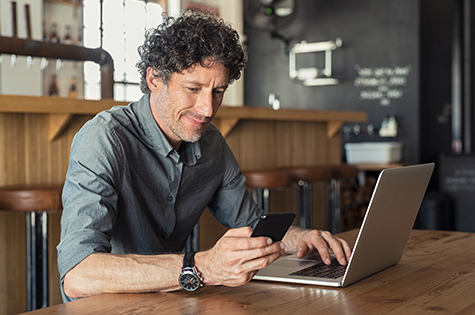 man sitting in cafe with laptop while looking at cell phone