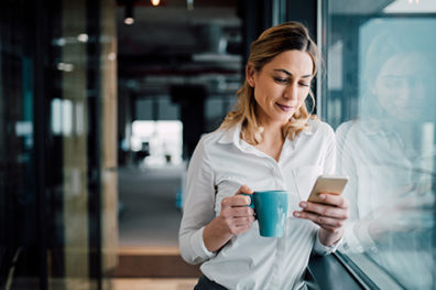 woman holding blue coffee mug while viewing phone screen